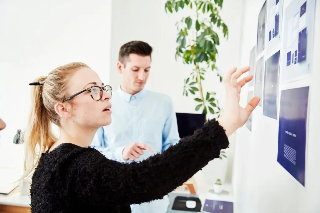 Two people looking at printed plans stuck on a wall, project management and discussions.